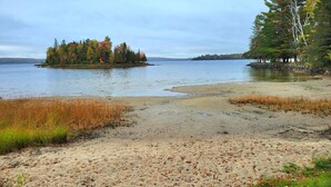 Une plage avec une petite île visible au loin, entourée d’eau et de végétation.