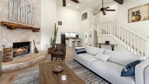 A spacious living room with a fireplace, a sofa, a coffee table, and a staircase. - Hoots Hollar Haus For 6 (Wimberley)