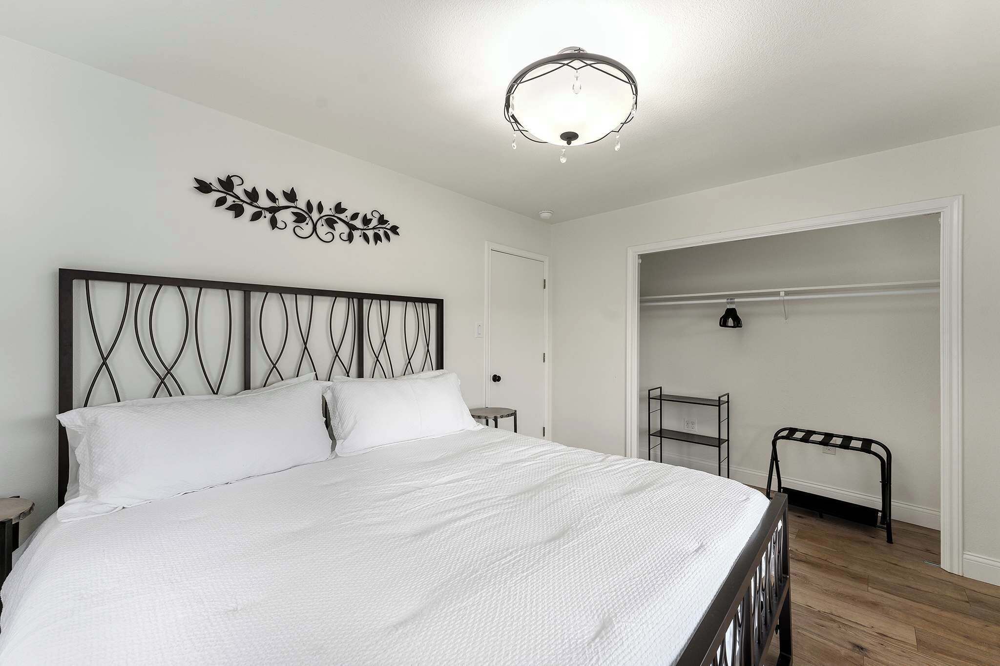 A neatly made bed with white linens, a decorative wall piece above it, and a closet with a hanging rack.