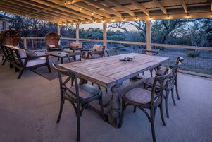 Un patio al aire libre con una mesa y sillas de madera, rodeado de mobiliario de mimbre y luces colgantes.