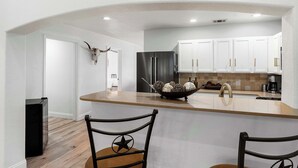 A modern kitchen with white cabinets, a black refrigerator, and a central island with a bowl of decorative items. - Hoots Hollar Haus For 6 (Wimberley)
