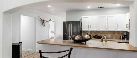 A modern kitchen with white cabinets, a black refrigerator, and a central island with a bowl of decorative items.