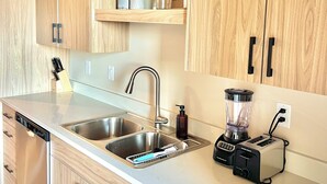 A modern kitchen with wooden cabinets, a stainless steel sink, a built-in toaster, and a blender.