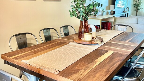 A dining area with a long wooden table, metal chairs, and two framed landscape paintings on the wall.