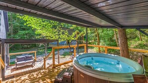 Eine Holzterrasse mit Whirlpool, einer Bank und Blick auf einen Wald.