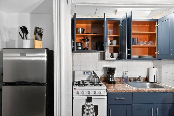 A kitchen with a stainless steel refrigerator, a gas stove, a coffee maker, and wooden cabinets.
