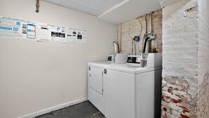 A laundry room with a washing machine and dryer, a brick wall, and posters on the wall.