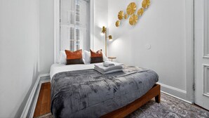 A bedroom with a bed, pillows, a bedside table, a lamp, and a window.