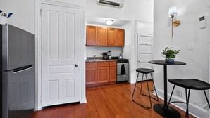 A compact kitchen with wooden cabinets, a refrigerator, an oven, and a small dining area with stools.