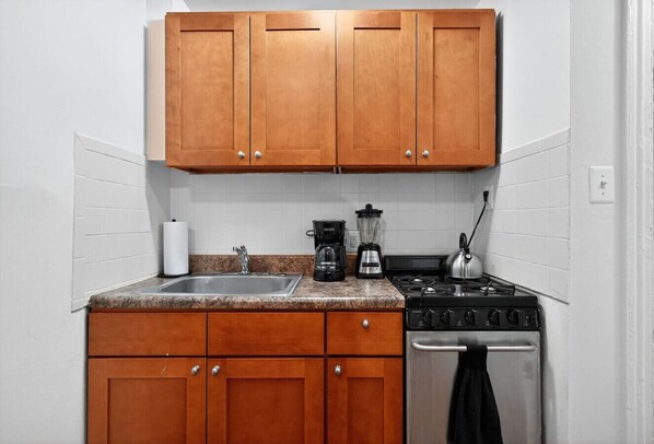 Una cocina con gabinetes de madera, encimera de granito, un lavabo, cafetera, hervidor y estufa.