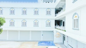 Un hôtel à plusieurs étages, avec des murs extérieurs blancs, de nombreux balcons et une place de stationnement bleue réservée aux personnes handicapées.