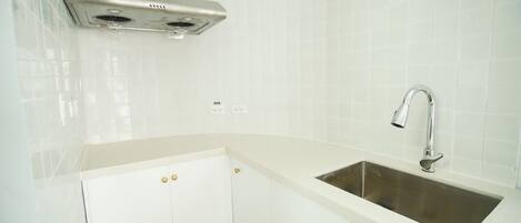 A kitchen with a stainless steel sink, white cabinets, and a ventilation hood.