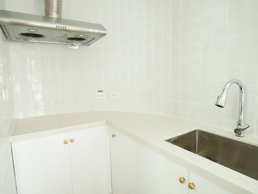 A kitchen with a stainless steel sink, white cabinets, and a ventilation hood.