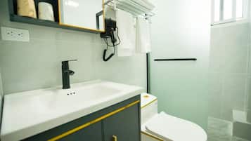 A bathroom with a white sink, black faucet, and a toilet. There is a towel rack with white towels and a hairdryer.