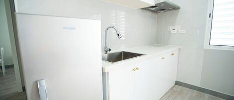 A modern kitchen with a stainless steel sink, white cabinetry, and a built-in range hood.