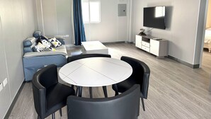 Un salon moderne avec une table ronde, des chaises noires, un canapé agrémenté de coussins à motifs, un téléviseur et un climatiseur fixé au plafond.