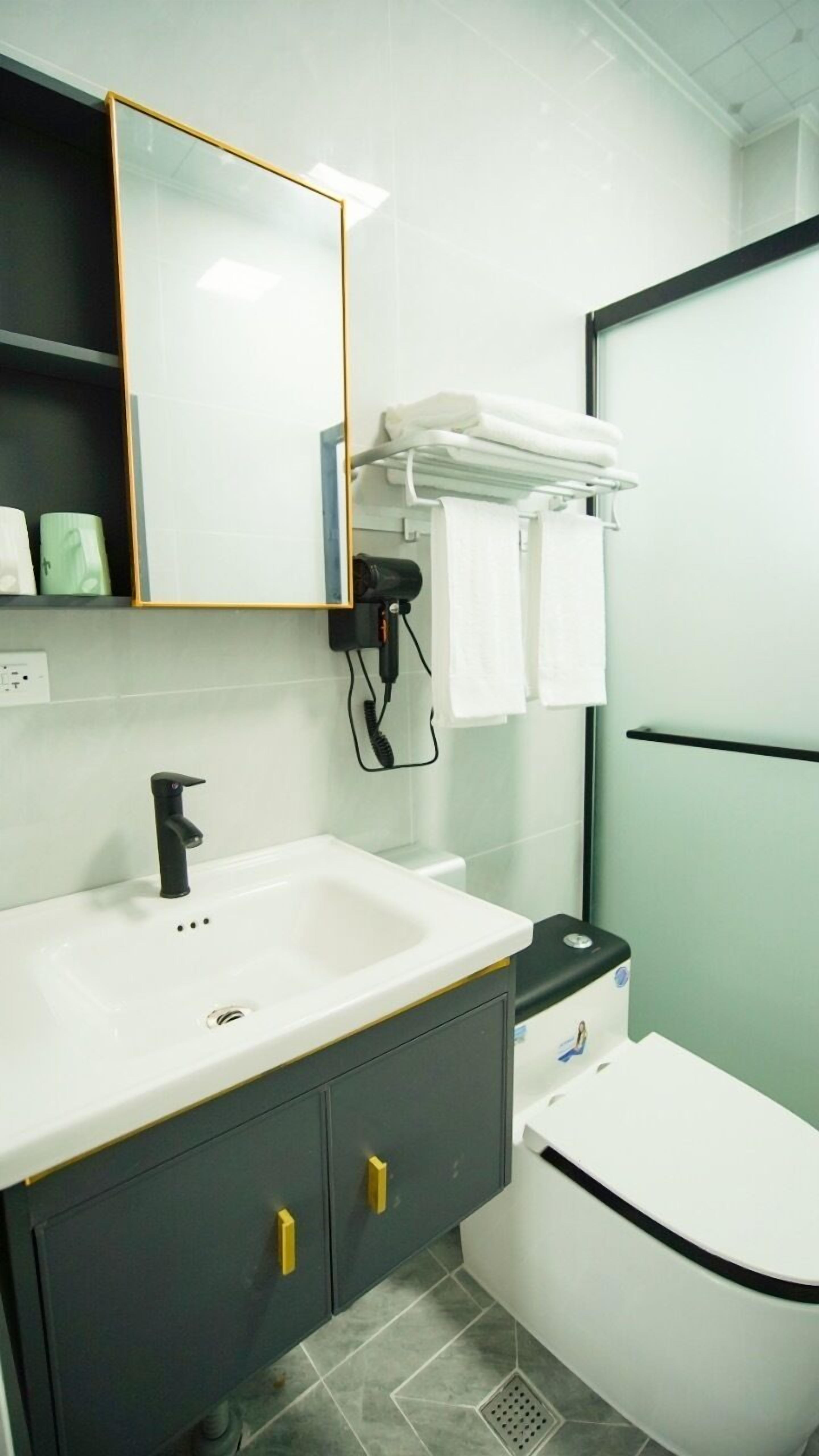 A modern bathroom with a white sink, dark cabinets, a mirror, and a toilet.