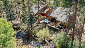 Une cabane dotée d’une terrasse, entourée d’arbres et bordée par un ruisseau.