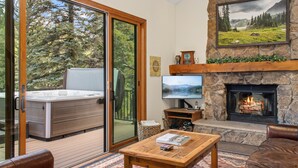 Un salon confortable avec une cheminée, un téléviseur et un jacuzzi situé à l’extérieur, juste derrière la porte-fenêtre coulissante.