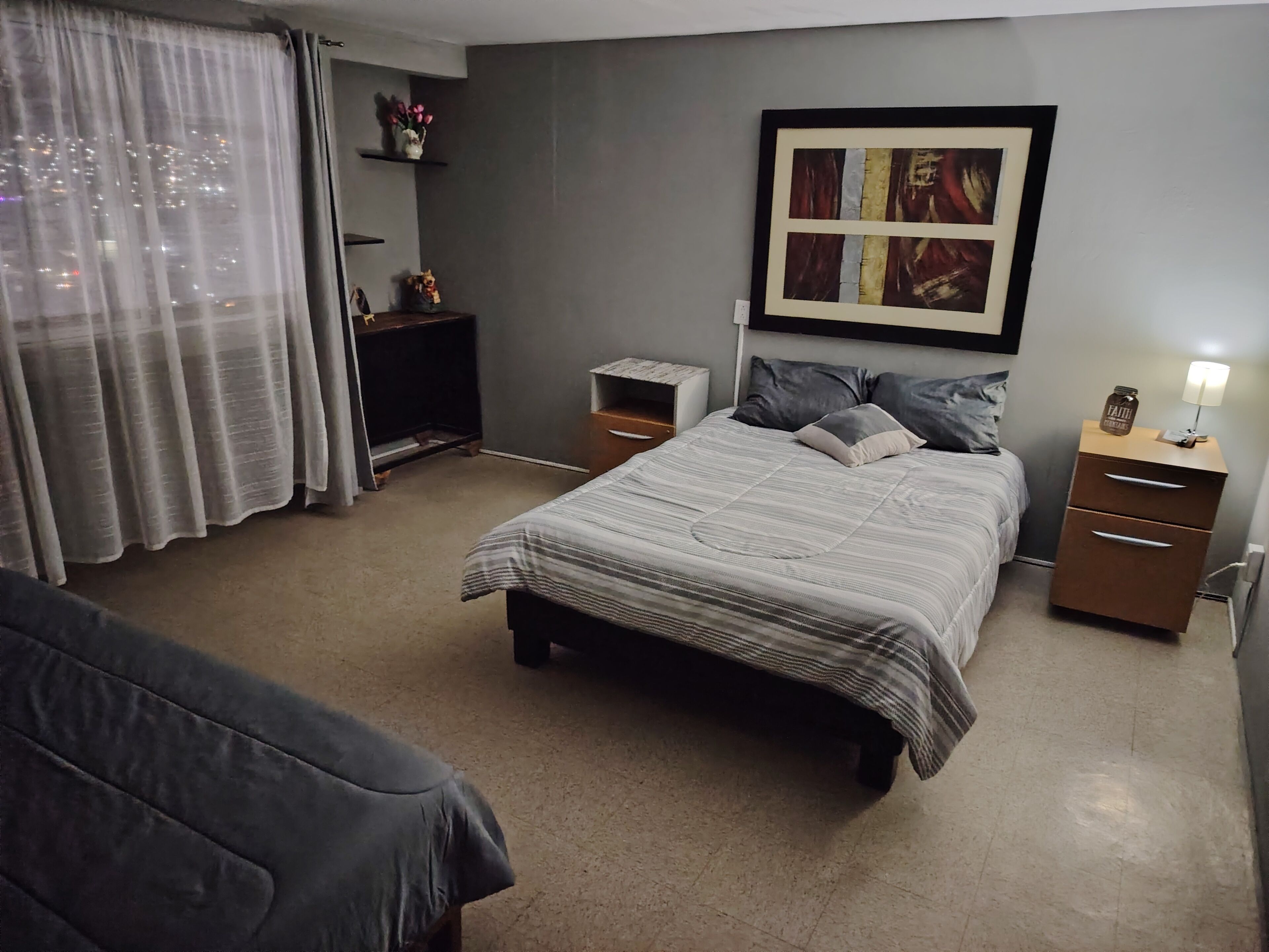 Una camera da letto con un letto, comodini, un appendiabiti, un armadio, una finestra con tende e un'opera d'arte a parete.