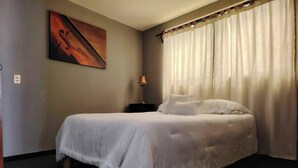 En snyggt bäddad säng i ett hotellrum, med ett litet sidobord, en lampa och en tavla på väggen.