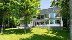 A modern two-story house with large windows, surrounded by a well-maintained lawn and trees. - Old Mission Peninsula Luxury on West Bay (Traverse City)