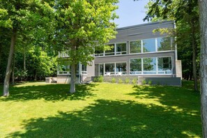 A modern two-story house with large windows, surrounded by a well-maintained lawn and trees.
