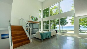 A spacious living area with a staircase, a sofa, and large windows overlooking a body of water. - Old Mission Peninsula Luxury on West Bay (Traverse City)