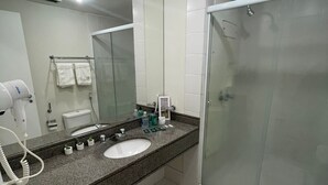 A modern bathroom with a granite countertop, a white sink, a mirror, a toilet, and a glass shower enclosure.