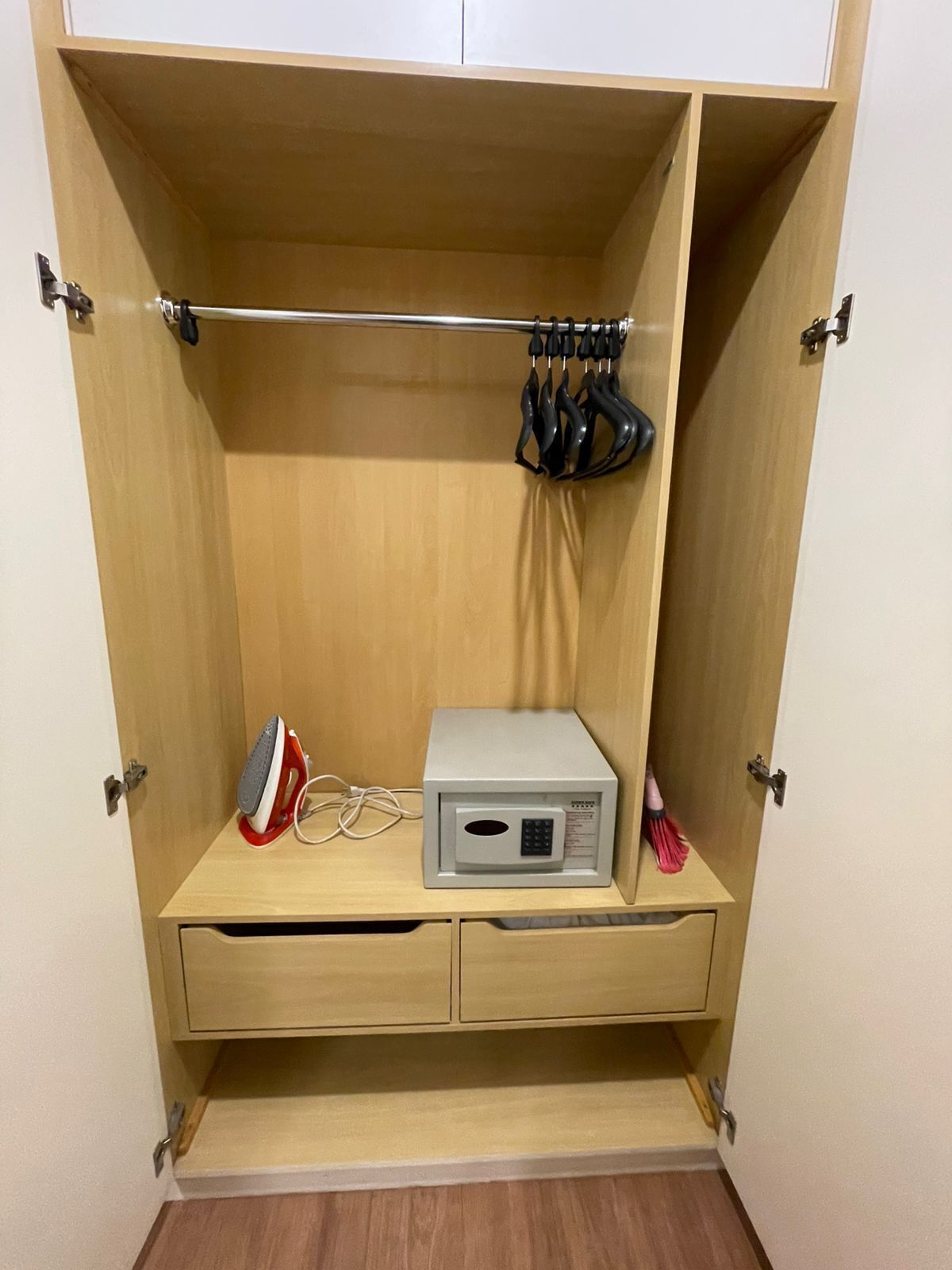Une armoire en bois équipée d’un four à micro-ondes, d’un fer à repasser et d’une tringle pour suspendre les vêtements.