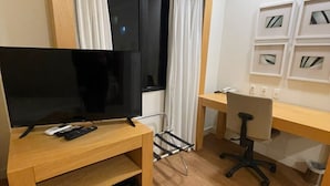 A compact hotel room with a wooden entertainment unit, a desk, and a chair.