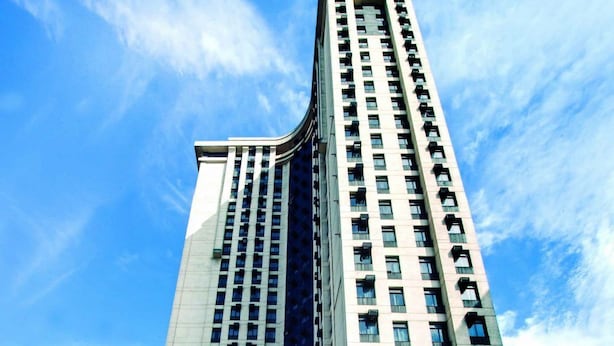A tall, modern hotel with a curved facade, multiple floors, and a prominent entrance with a covered area.