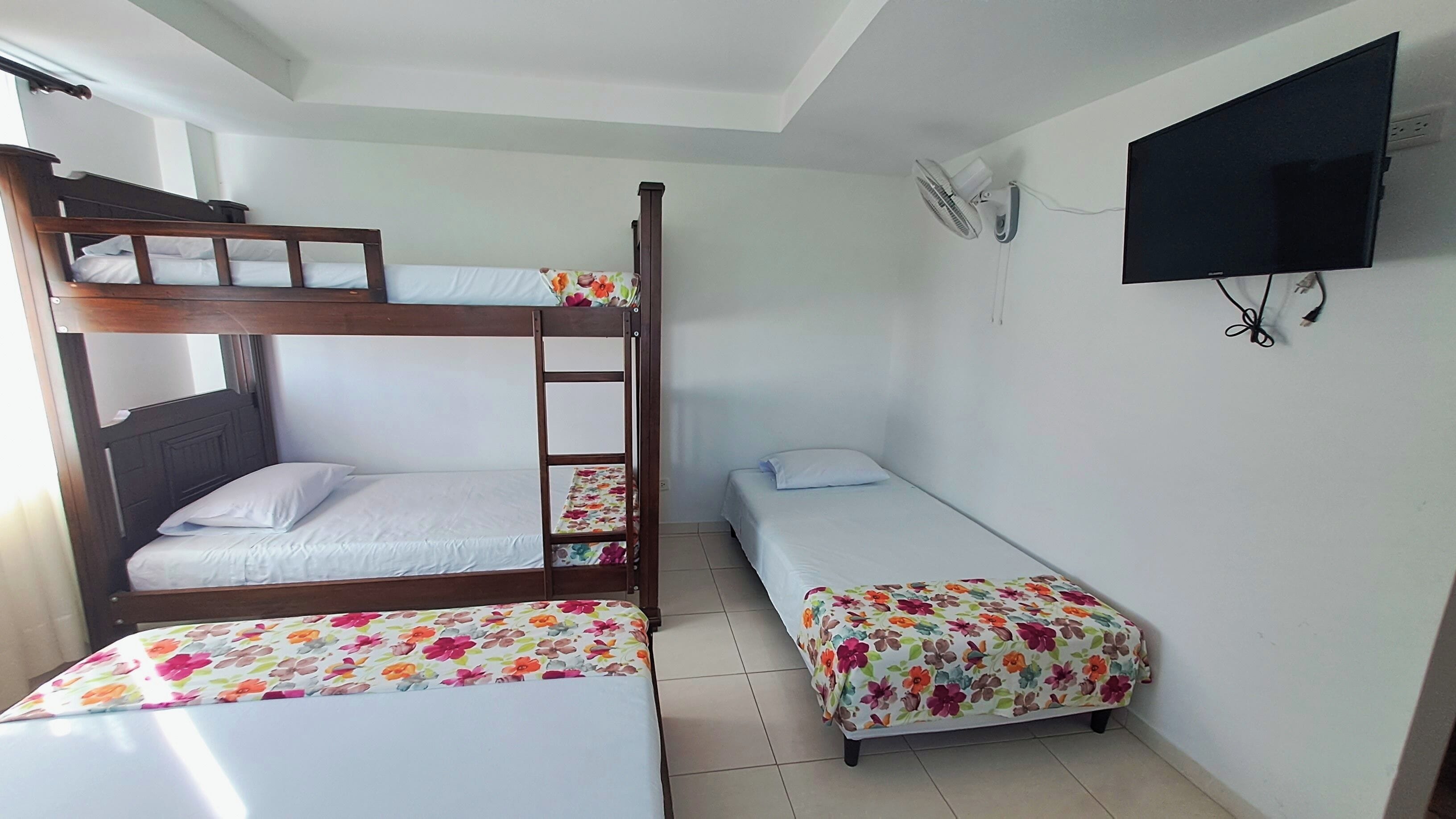 Un dormitorio con literas, una cama individual, un televisor y un ventilador.