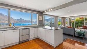 A modern kitchen with large windows, a wooden floor, and a view of the sea. - Panorama Terrace: Lake Views, Deck & Walk to Town (Queenstown)