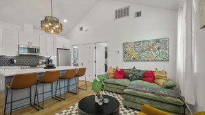 A modern kitchen with white cabinets, a bar area with stools, a dining table, and a large decorative plant.