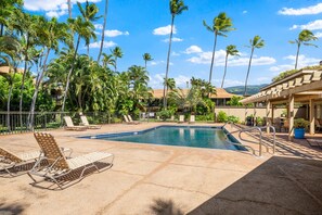 A pool area with lounge chairs, palm trees, and a clear blue sky.