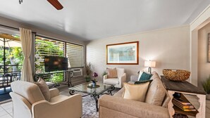A living room with a glass coffee table, beige sofas, a TV, and a painting on the wall.