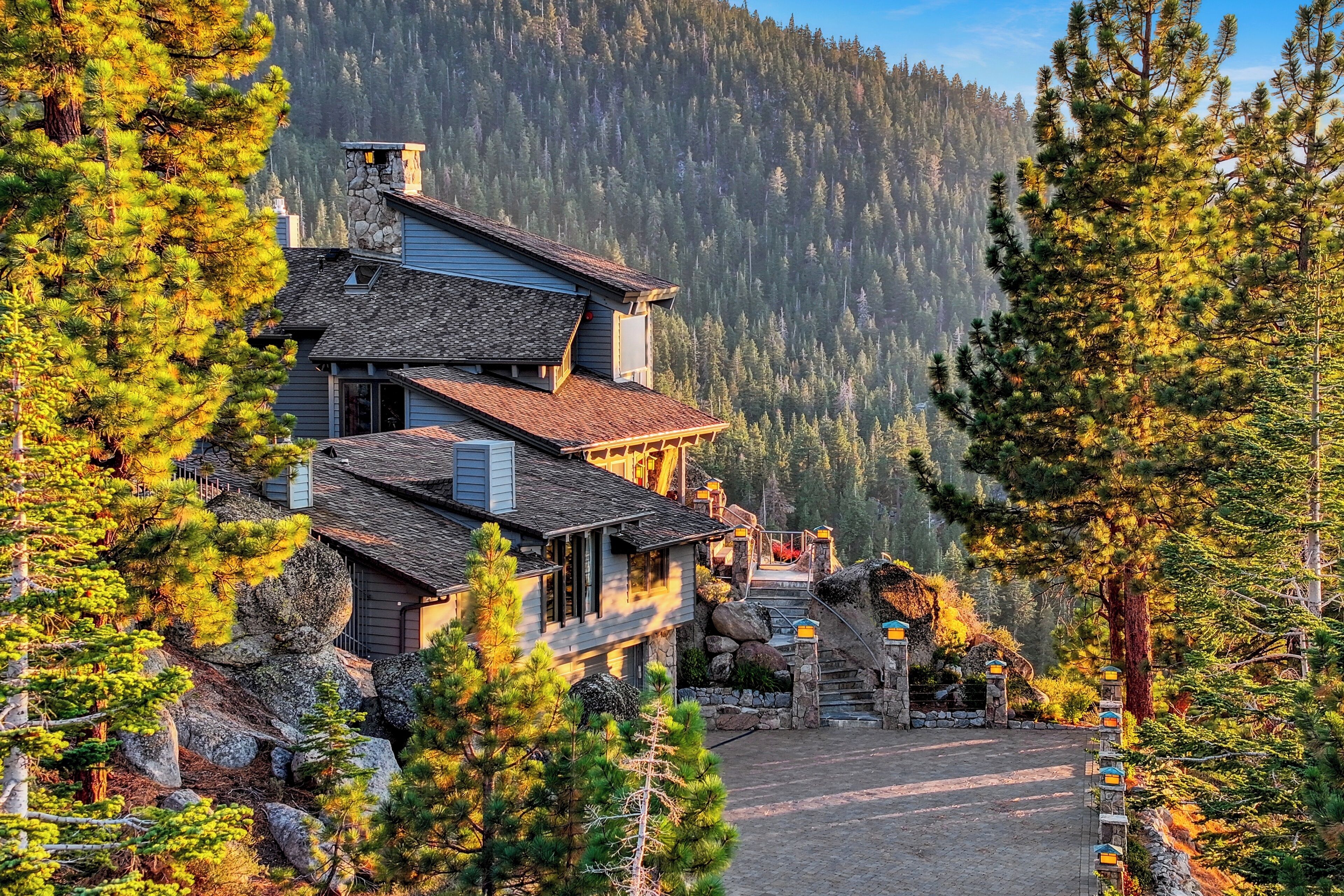 Ein mehrgeschossiges Haus mit einem Steinkamin, umgeben von Kiefern und einem Berg im Hintergrund.