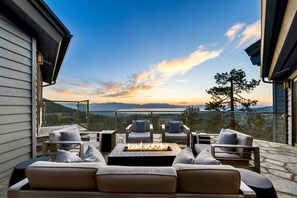 A modern outdoor seating area with a fire pit, overlooking a scenic mountain view during sunset.