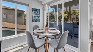A dining area with a round table, grey upholstered chairs, and a clear view of the outside. - A-Wave From It All, Steps to Sand with AC! (San Diego)