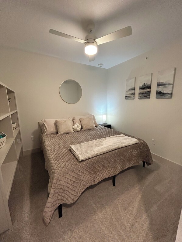 Une chambre à coucher comprenant un lit, un ventilateur de plafond, un miroir rond et trois tableaux accrochés au mur.