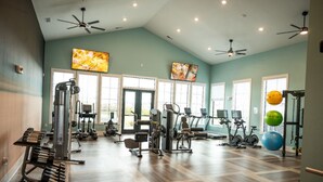 A spacious gym with various exercise equipment, large windows, and ceiling fans. - Relaxing 1 BR Retreat w Resort Amenities  (Waukee)
