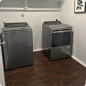 Two compact, grey, wall-mounted laundry machines in a corner with a wooden floor and a white wall.