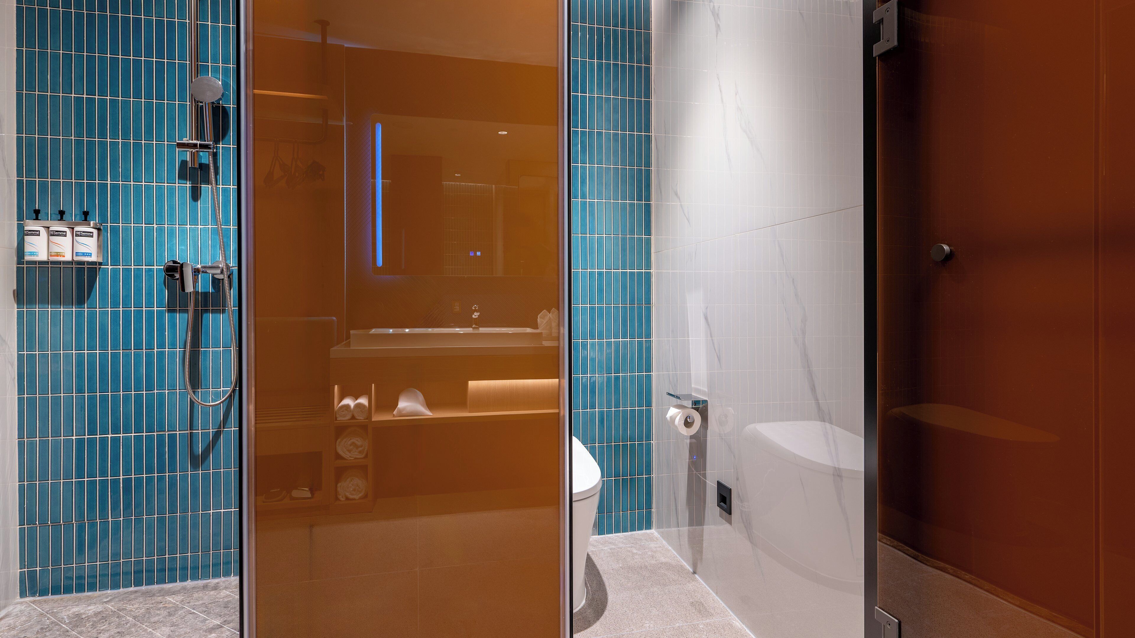 Un baño moderno con cabina de ducha de vidrio, inodoro blanco y pared con azulejos azules.