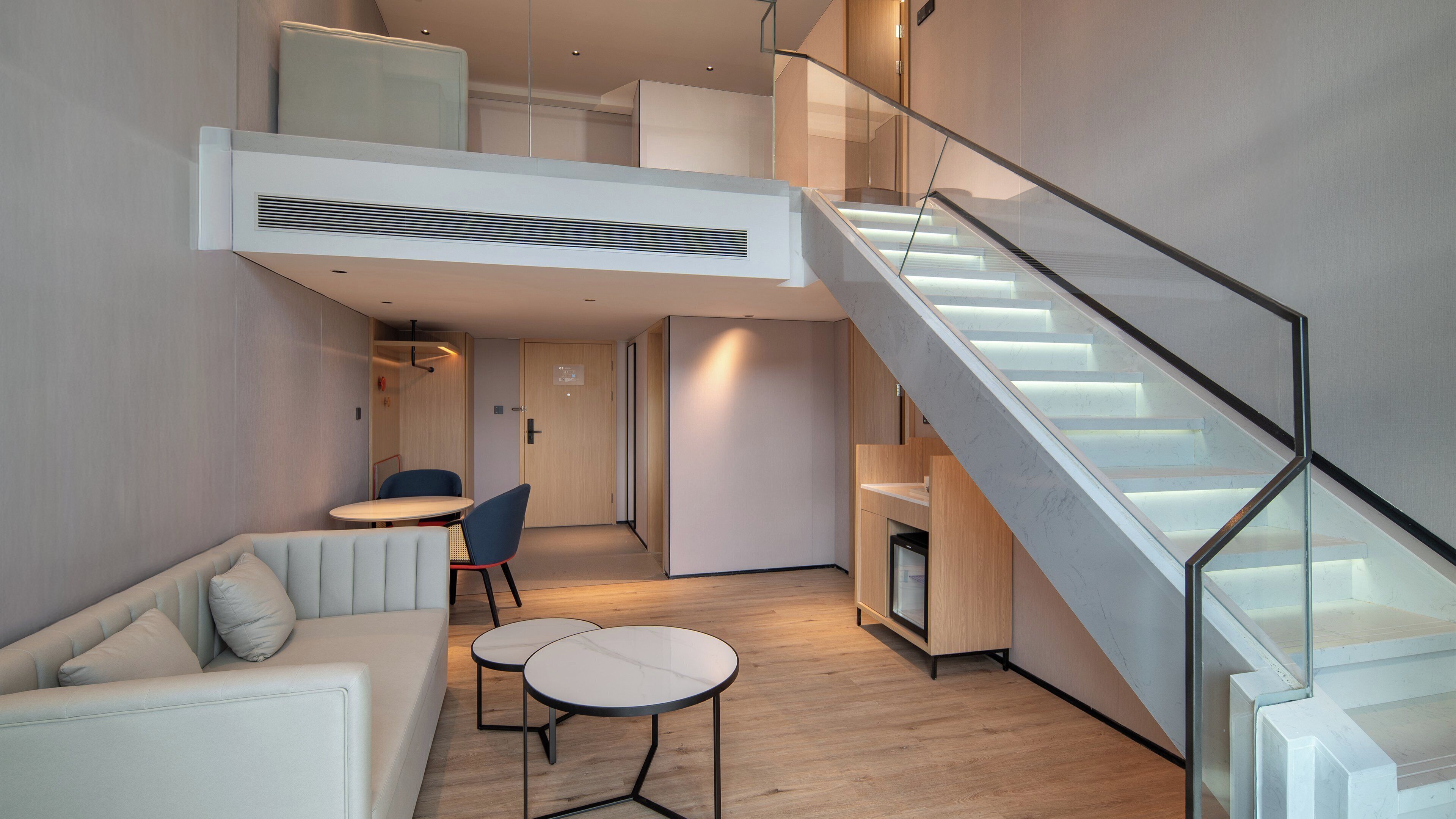 A modern interior with a loft-style bed, a staircase, and a seating area with a table and chairs.