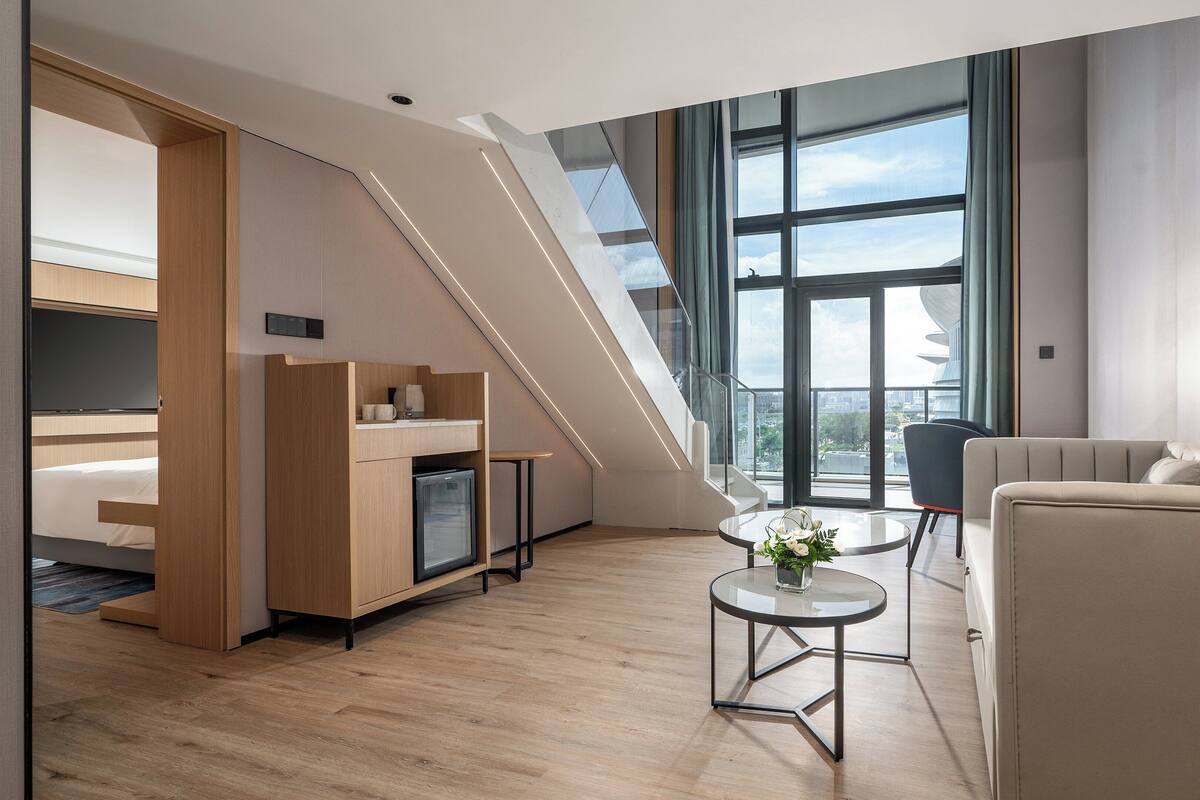 A modern hotel room with a lofted sleeping area, a dining table, and a sofa.