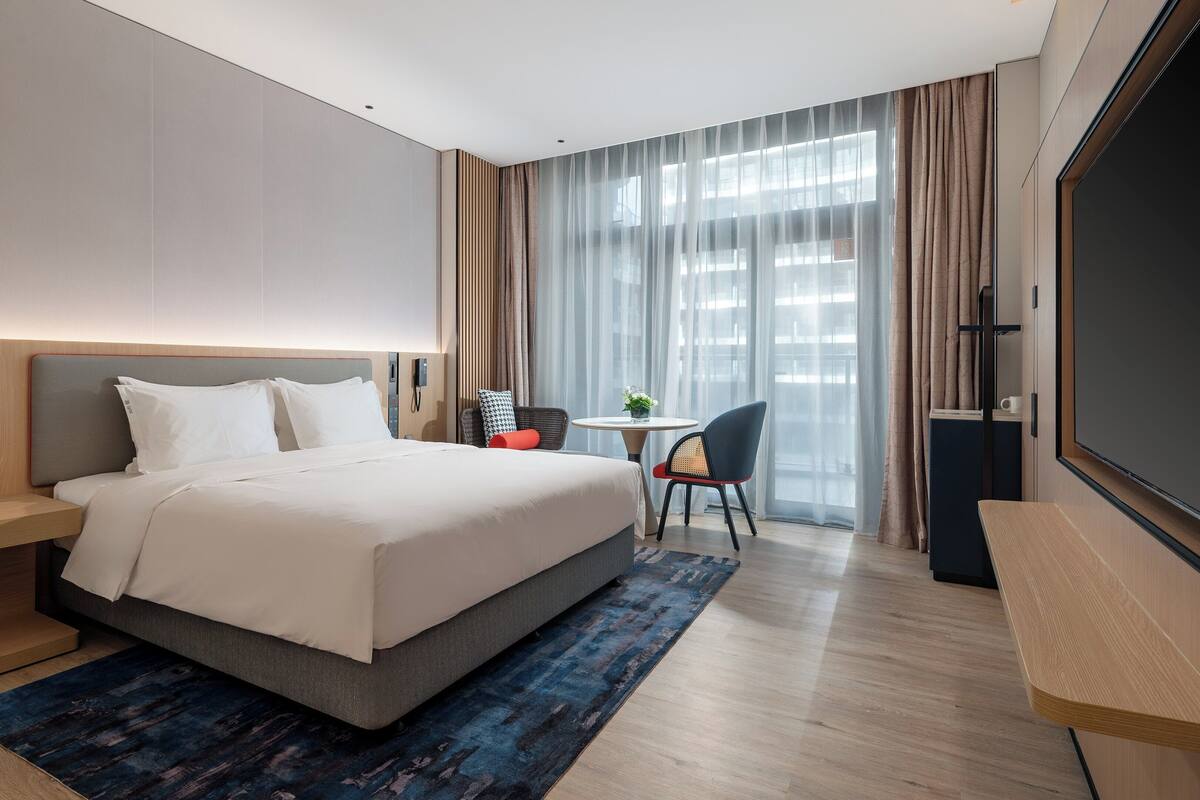 A modern hotel room with a large bed, a desk, a chair, and a TV.
