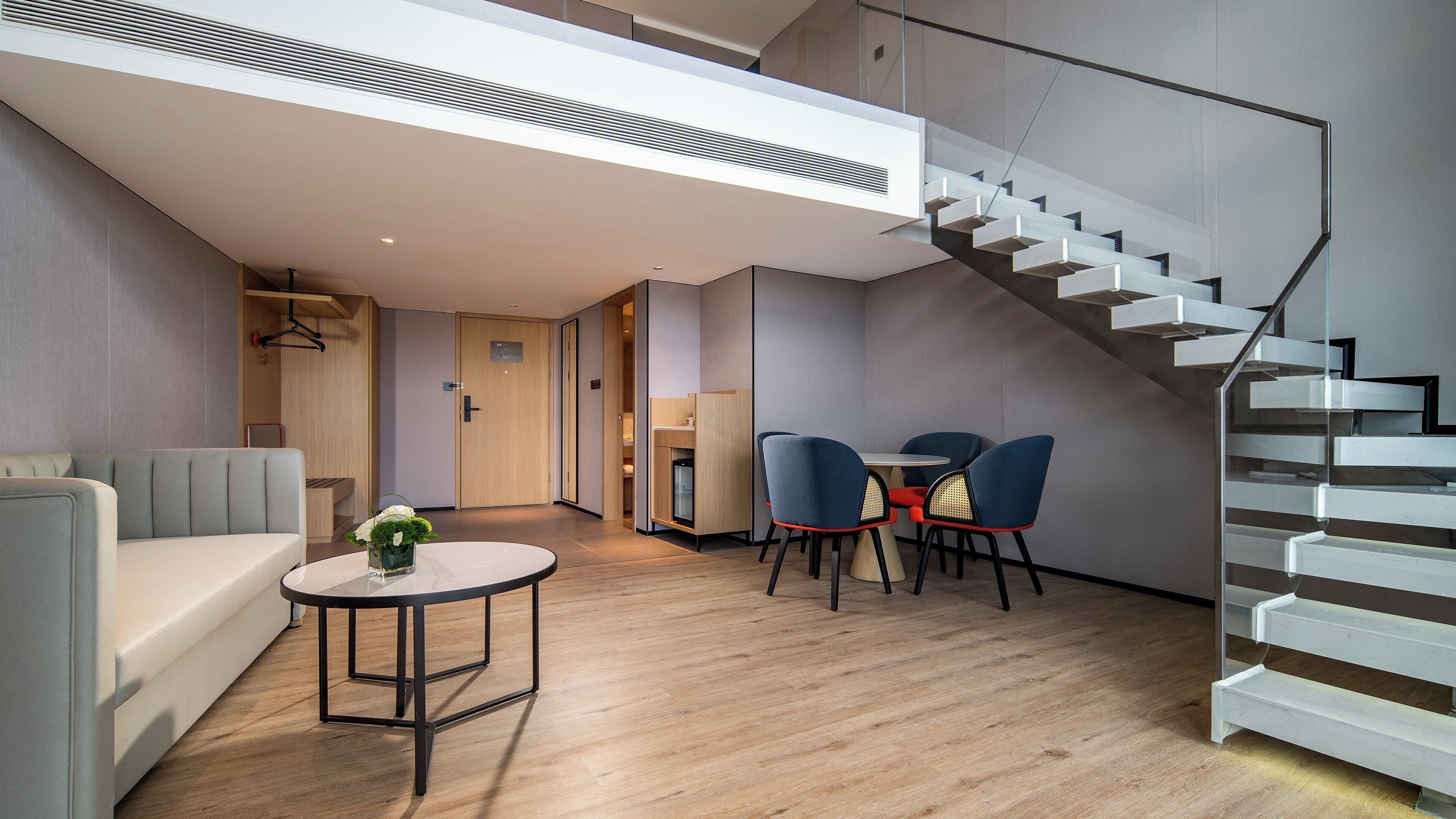 A modern interior with a staircase, a sofa, a table with chairs, and a small kitchenette.
