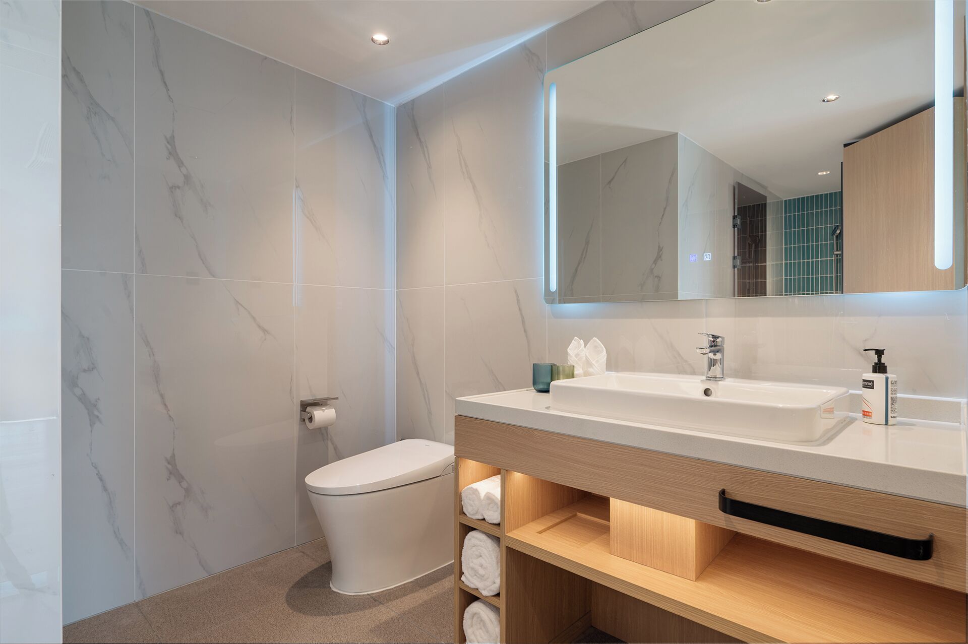 Et moderne badeværelse med en marmorvæg, toilet, håndvask med spejl og en hylde med håndklæder.