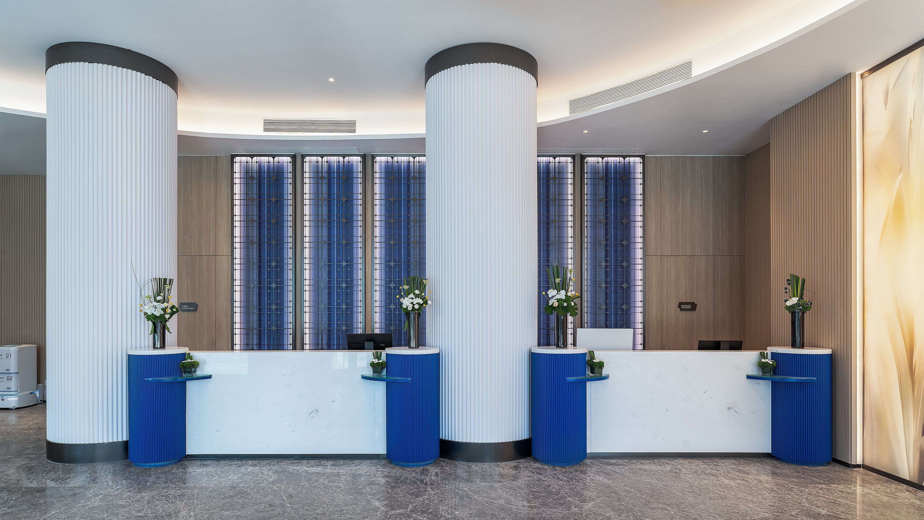 A reception area with a modern design, featuring tall white columns, a reception desk, and decorative vases.